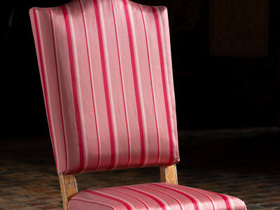 A reddish-pink upholstered side chair with vertical red stripes and gilt gold legs. 