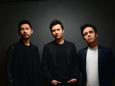 Three young men with dark hair, wearing suit jackets, looking directly at the camera 